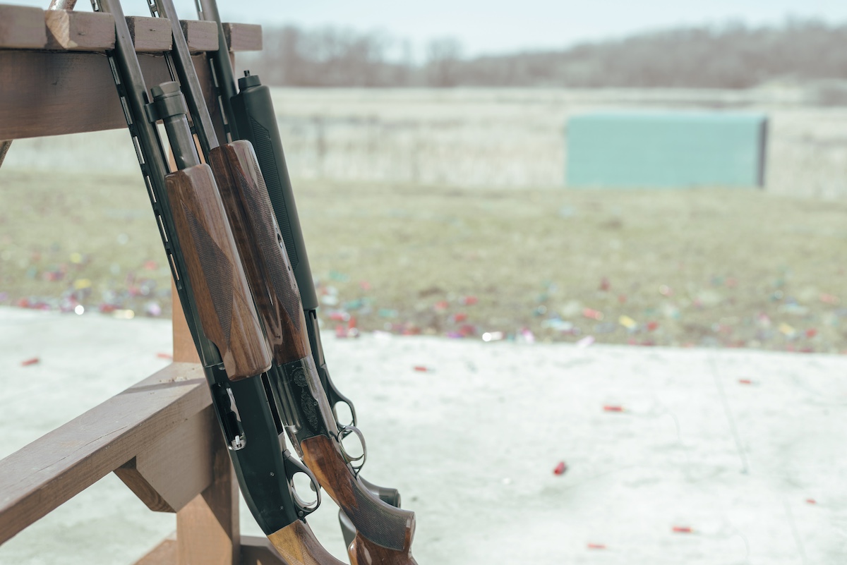 close up of shot guns placed on rack, with shell casings seen on the floor.